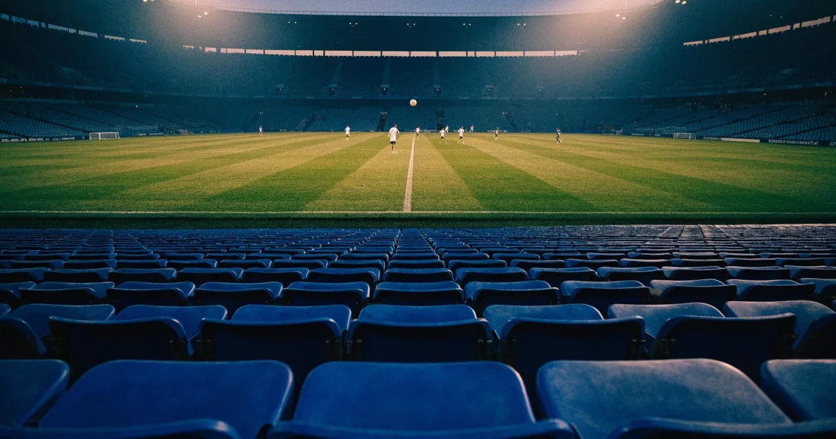 Leere Sitzreihen eines großen Stadions unter Flutlicht, dahinter die ferne Sicht auf den hell beleuchteten Rasen nach Sonnenuntergang.