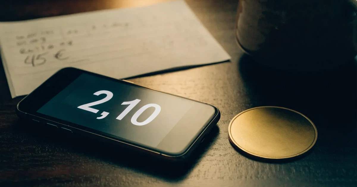 Eine einzelne goldfarbene Münze ohne Prägung liegt auf einem dunklen Tisch, daneben ein ausgeschaltetes Smartphone.