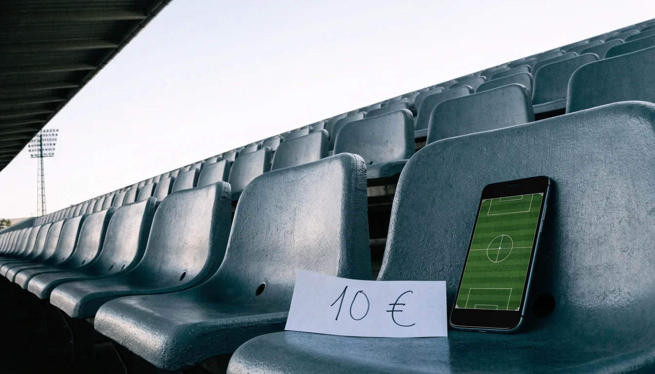 Eine leere Tribüne eines Fußballstadions bei Tageslicht, Sitzschalen in Reihen und dahinter ein Flutlichtmast.