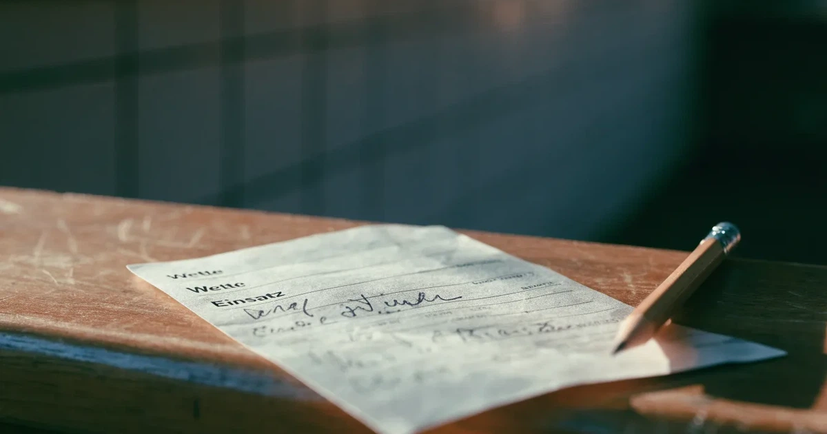 Ein leerer Wettschein aus Papier liegt neben einem Stift auf einer hölzernen Theke, weiches Licht fällt von der Seite ein.