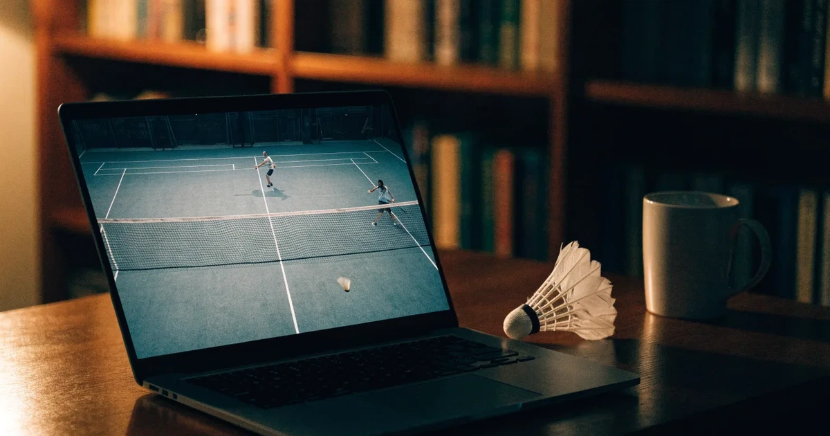 Eine leere Badmintonhalle mit gespanntem Netz und hellen Hallenlichtern, ein Federball liegt auf dem Hallenboden.