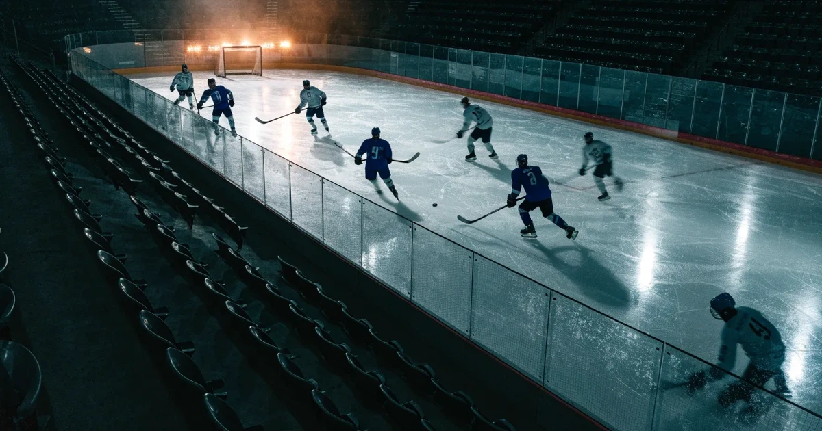 Eine Eishockeyhalle von der Tribüne aus gesehen, spiegelglatte Eisfläche, Banden ohne Schriftzüge, helles Flutlicht.